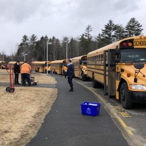 Bus drivers line up to receive the meals, which they will distribute to students along their regular bus routes. Transportation Director Julie Waters oversees the logistics. (Photo by Lynda Clancy)