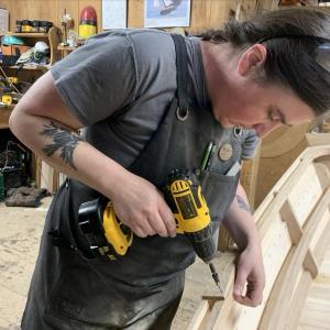 Emma and her almost completed skiff. Here, she’s drilling the fastener holes to be able to attach the oarlock pads to the hull. (Photo by Nate Hathaway)