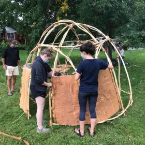 Wabanaki artist Barry Dana watches as high school students add sides to the ten-foot traditional wigwam lodge on the west lawn of the Skowhegan History House Museum and Research Center. (Photo by Susan Cochran/courtesy History House)