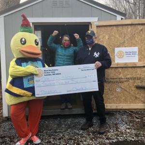 Lucky the Duck and West Bay Rotarian Ray Fink present a check to One Less Worry’s Executive Director Sharon Hobson (in front of the shed that was donated to OLW by West Bay Rotary). (Photo courtesy West Bay Rotary)