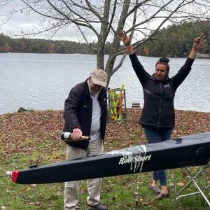 Rob Short pours champagne over the new boat while Executive Director Anna Goodale cheers him on.