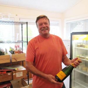 Chef Michel Hetuin co-owner of Chez Michel Restaurant and its newly converted Beach Inn Market, displays one of his favorite champagnes, Veuve Clicquot. Behind him is their collection of wines for sale. Photo by Kay Stephens