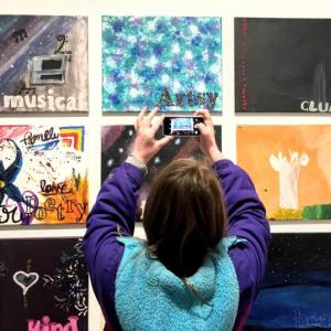 A young artist snaps a photo of their artwork hung on a gallery wall during the Young Artist Gallery Takeover. Photo courtesy of Waterfall Arts.