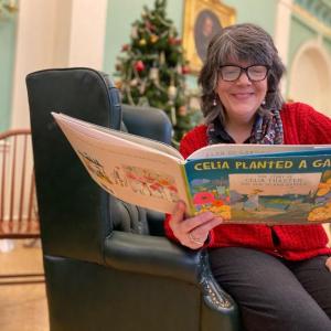 Stephanie Holman, children’s librarian, Belfast Free Library, enjoys one of the gardening books for kids donated by Belfast Garden Club. (Photo courtesy Belfast Garden Club)