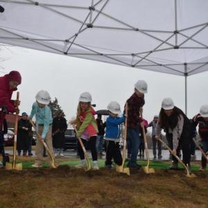 Ceremonial gold shovels push the starting layer of dirt that will one day become the CTE/Makerspace building at St. George School. From left to right: Diana Bean, Ella Walvatne (3rd grade), Luna Waters (2nd grade), Gunnar Jeffers (PreK), Ben Lord (6th), Olivia Myers (8th), and Byron Marves (5th). (Photo by Sarah Thompson)