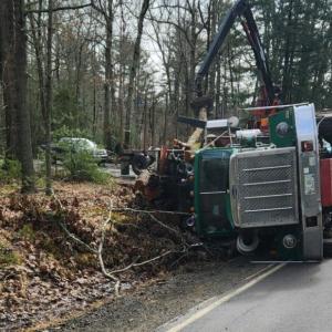 The driver of a loaded logging truck was able to climb out of the cab after it went onto its side on Route 105, March 6, in Camden. (Photo courtesy Camden Fire Dept.)