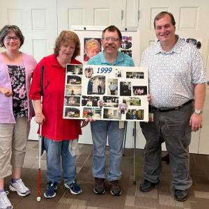 From left, Retta Goughnour, BillieJo Stewart, Jared Stewart, and John Paul Carr pose with a poster showcasing memories from 1999 during the 25th anniversary celebration of Bank of America’s Belfast Support Services. (Photo courtesy Bank of America)