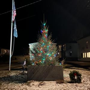 A short lit Christmas tree in front of a stone monument to War Veterans