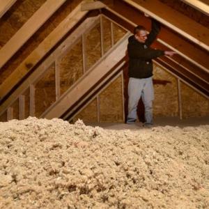 Michael McDonald, site supervisor at a new subdivision in Gorham, points out a detail in an attic filled 14 inches deep with blown cellulose insulation. Maine’s new energy code requires an unprecedented level of attic insulation, triggering a debate over balancing efficiency and housing affordability. Photo by Fred J. Field. a man standing in an attic.