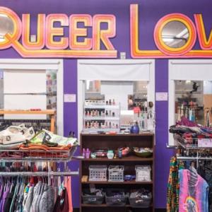 a look inside a thrift store, with a sign reading queer love hanging on the wall.