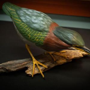 Colorful decorative wooden decoy of blue winged teal green heron mounted on driftwood