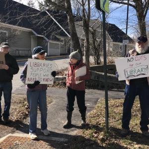 A group of protestors hold signs supporting local libraries