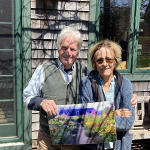 Barbara and Elliot are holding a painting of the garden in high season.