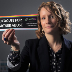 regina rooney holds a bumper sticker that reads no excuse for partner abuse