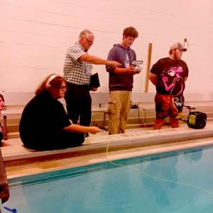 Four people at side of pool in lighted room, one holding remote control