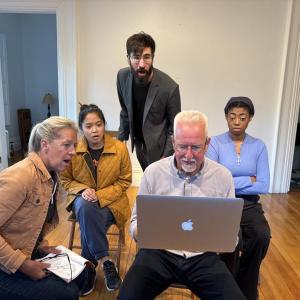 Four people look at a laptop with various expressions on their faces