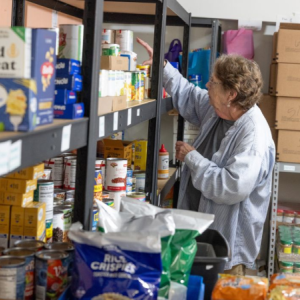 Phylis Allen organizes supplies at Neighbor’s Cupboard, a food pantry in Winterport, Maine, that she has helped run for the past 17 years. Photo by Katherine Emery. A woman reaches for an item on a shelf.