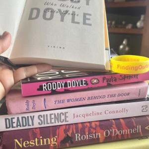 The autographed and first-edition copy of Roddy Doyle's The Woman Who Walked Into Doors that tops this stack was a gift to the nonprofit's CEO+Founder Patrisha McLean from her son Wyatt. The Irish authors of all of these books will be joining talks with Finding Our Voices through March. (Photo by Patrisha McLean) Stack of books with one book open to autograph on first page