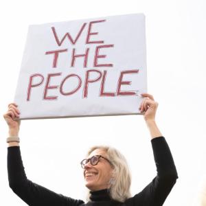 Female protestor holds a sign "We the People"