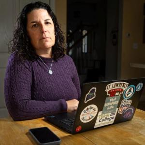 Carrie Woodcock, executive director of the Maine Parent Federation, sits at her kitchen table in Saco on October 23, where she works most days. Woodcock's organization provides free information, training and support to families of children with disabilities or special health care needs. She said she found declining school performance among students with disabilities and low incomes unsurprising, though she cautioned that testing doesn’t always show what students have learned. Photo by Troy R. Bennett. carrie woodcock sitting at a table.