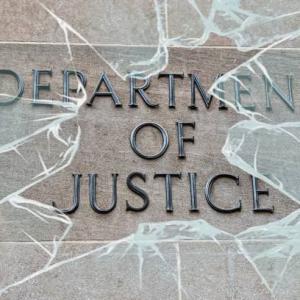 Department of Justice sign behind broken glass