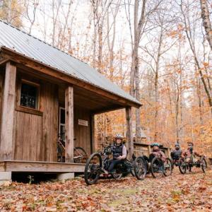 Four people ride adaptive mountain bikes toward a structure