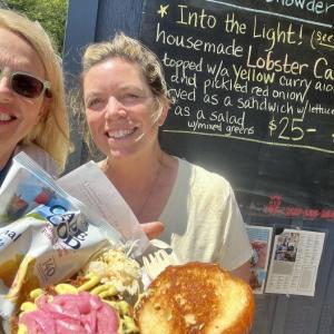Selfie picture of two women holding a tray of food in front of a menu board