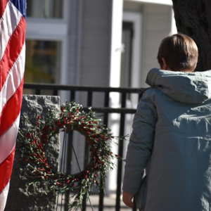 Girl observes wreath attached to monument, to the side a flag