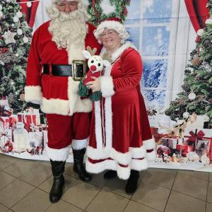Santa and Mrs. Claus standing in front of decorated trees, window