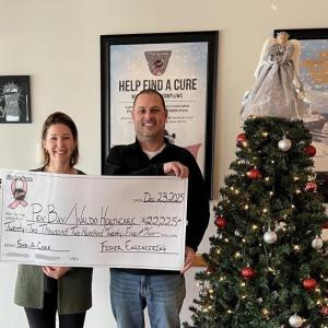 Woman and man hold oversized check next to Christmas tree