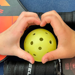 Hands shaped into hearts over a pickleball and paddles