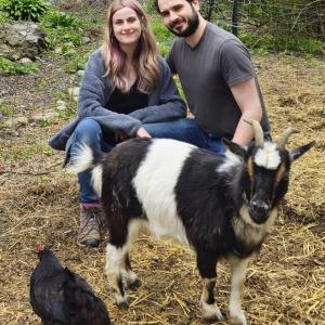 woman and man squat for photo with goat and chicken