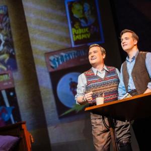 Two men stare off into the distance in front of comic book covers