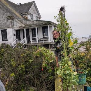female holds up vine of vegetation in front of house
