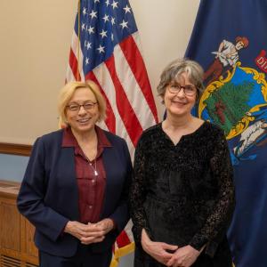 two women pose in front of state, federal flags