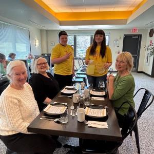 Students wearing yellow shirts serve a group of women