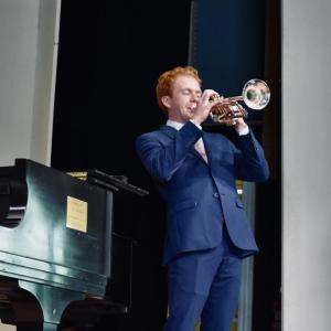 male in blue suit plays trumpet