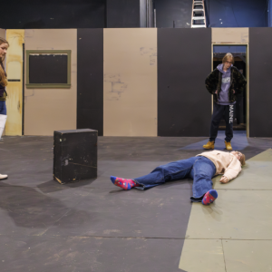 two people standing, one person laying on floor