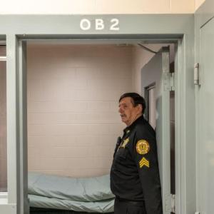 A corrections officer stands to the side in a doorway. 