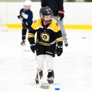a boy is learning to skate and move a puck on ice at Midcoast Rec.