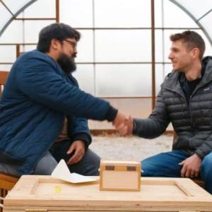 two men shake hands in an empty greenhouse